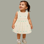 Pastel yellow sleeveless cotton frock with mint green embroidery and pleated skirt for baby girls, displayed on a white fur background with floral basket hanger.