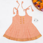 Peach silk Onam knot frock with zari border & triangle yoke. Ages 0–12M. Elegant festive outfit for baby girls.
