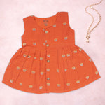 Baby girl in a vibrant orange ethnic sleeveless frock by Boon Babies, showing intricate traditional embroidery and fabric details.