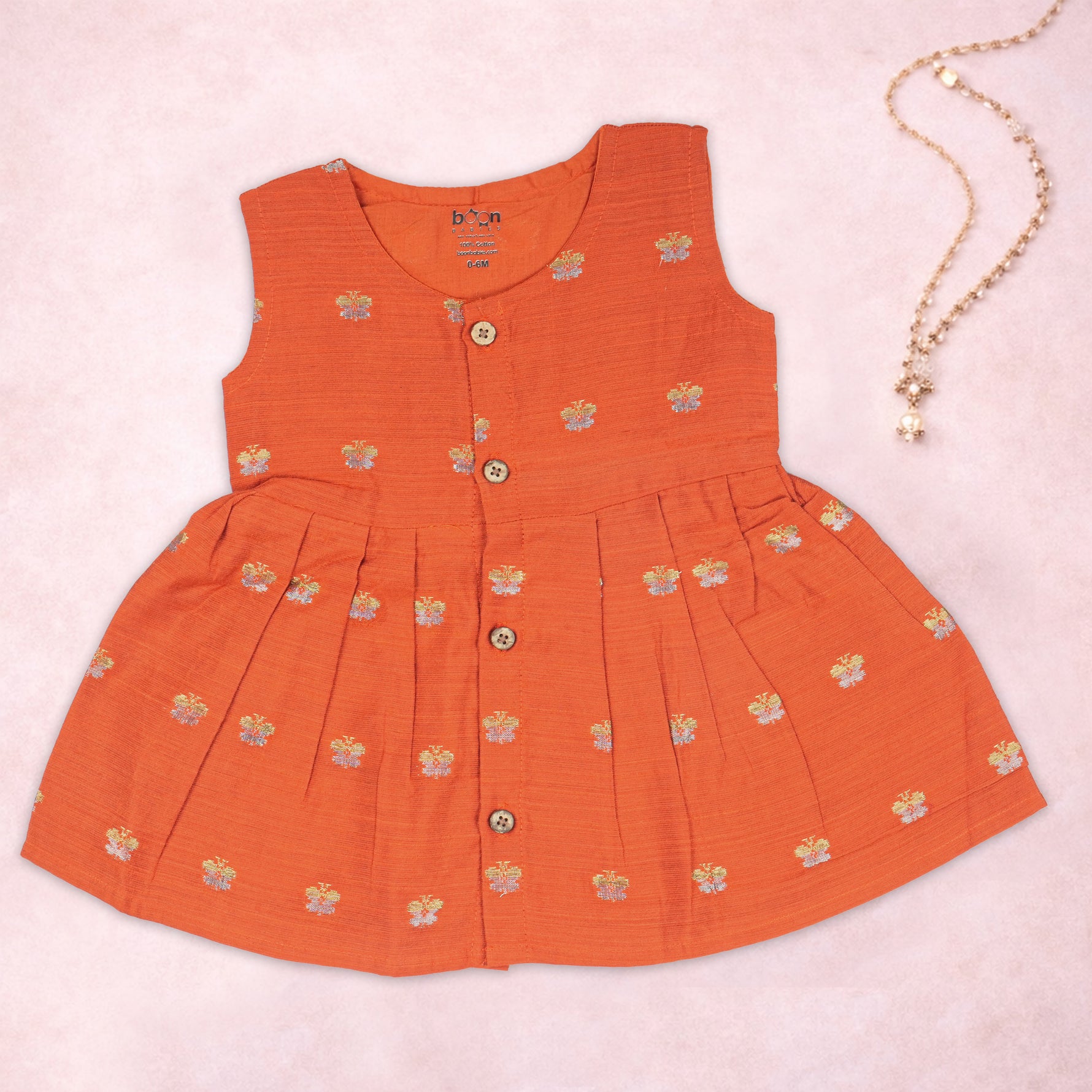 Baby girl in a vibrant orange ethnic sleeveless frock by Boon Babies, showing intricate traditional embroidery and fabric details.
