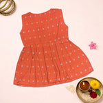 Baby girl wearing a bright orange Boon Babies ethnic sleeveless frock with traditional embroidery and ruffle details.
