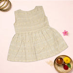 Baby girl in a premium ivory ethnic sleeveless frock by Boon Babies, featuring traditional design and delicate fabric.