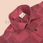 Folded rose pink silk shirt with golden grid pattern, placed beside a white veshti – boys' traditional festive wear from Boon Babies, Coimbatore.