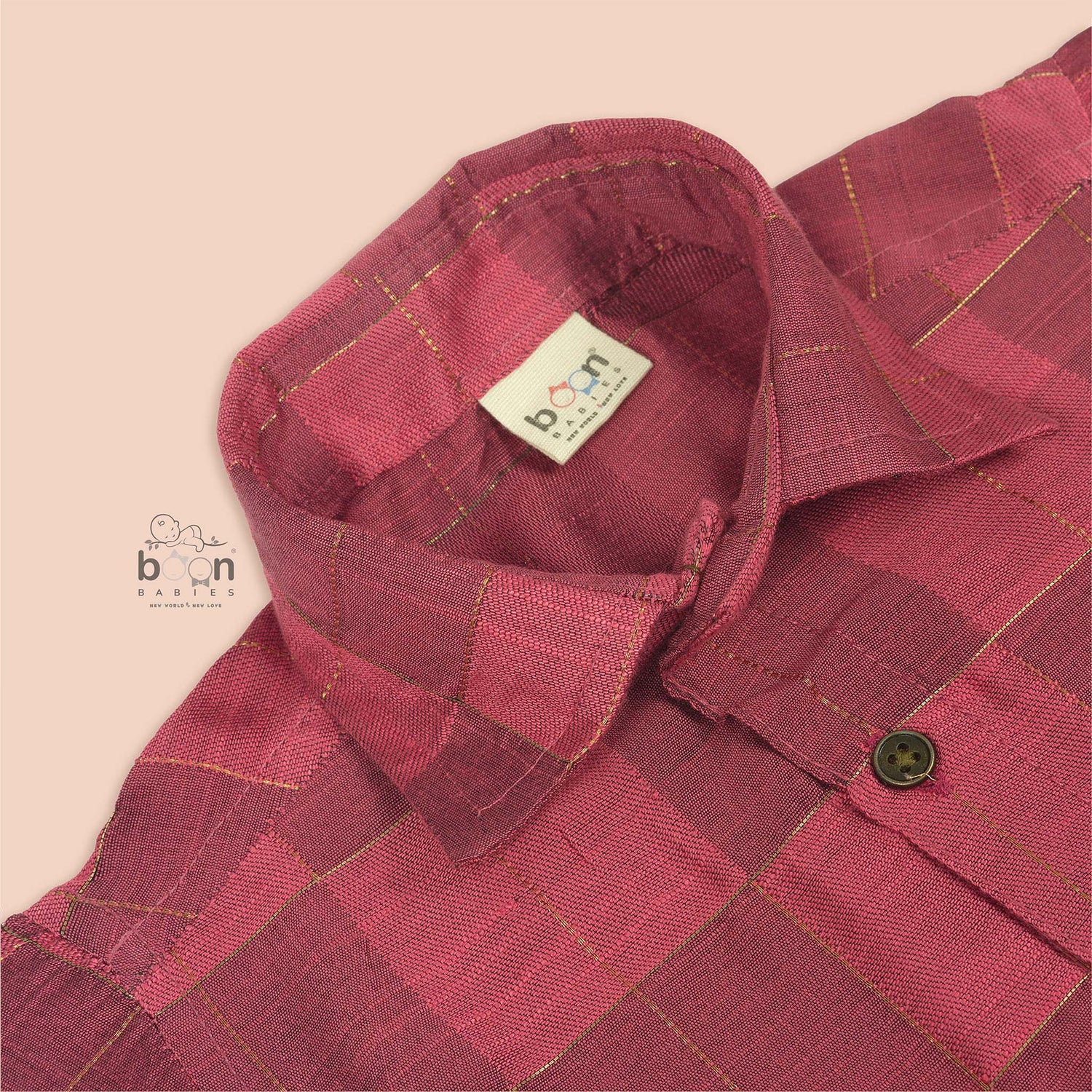 Folded rose pink silk shirt with golden grid pattern, placed beside a white veshti – boys' traditional festive wear from Boon Babies, Coimbatore.