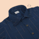Boys navy blue silk shirt with subtle gold stripes, folded beside a white and gold pattu dhoti – Boon Babies festive wear.