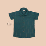 Teal green silk shirt for boys with gold vertical detailing, neatly paired with traditional white pattu dhoti – festive wear set by Boon Babies.

