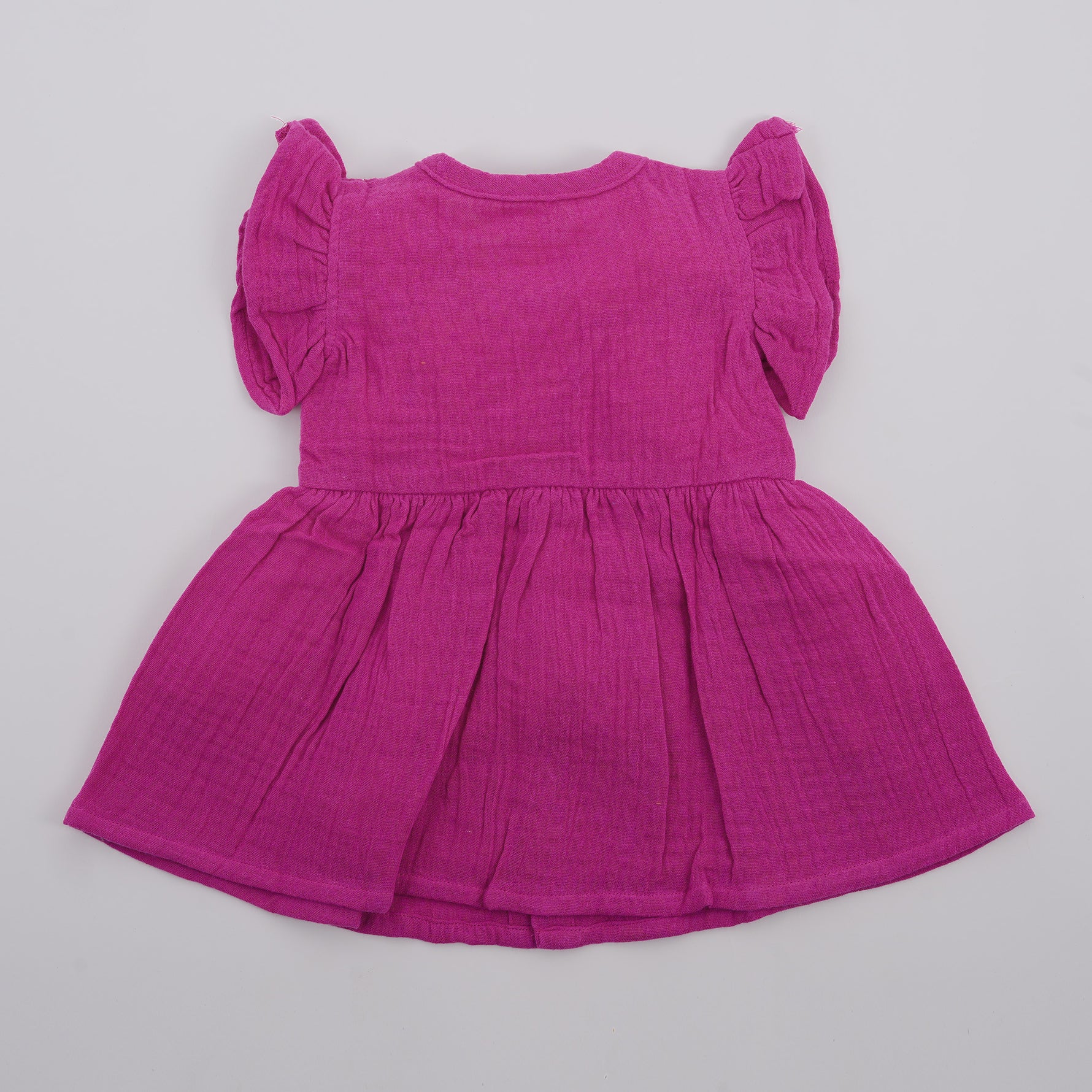 Back view of a baby's magenta-purple crinkled muslin solid frill frock by Boon Babies, featuring ruffled details and soft fabric.
