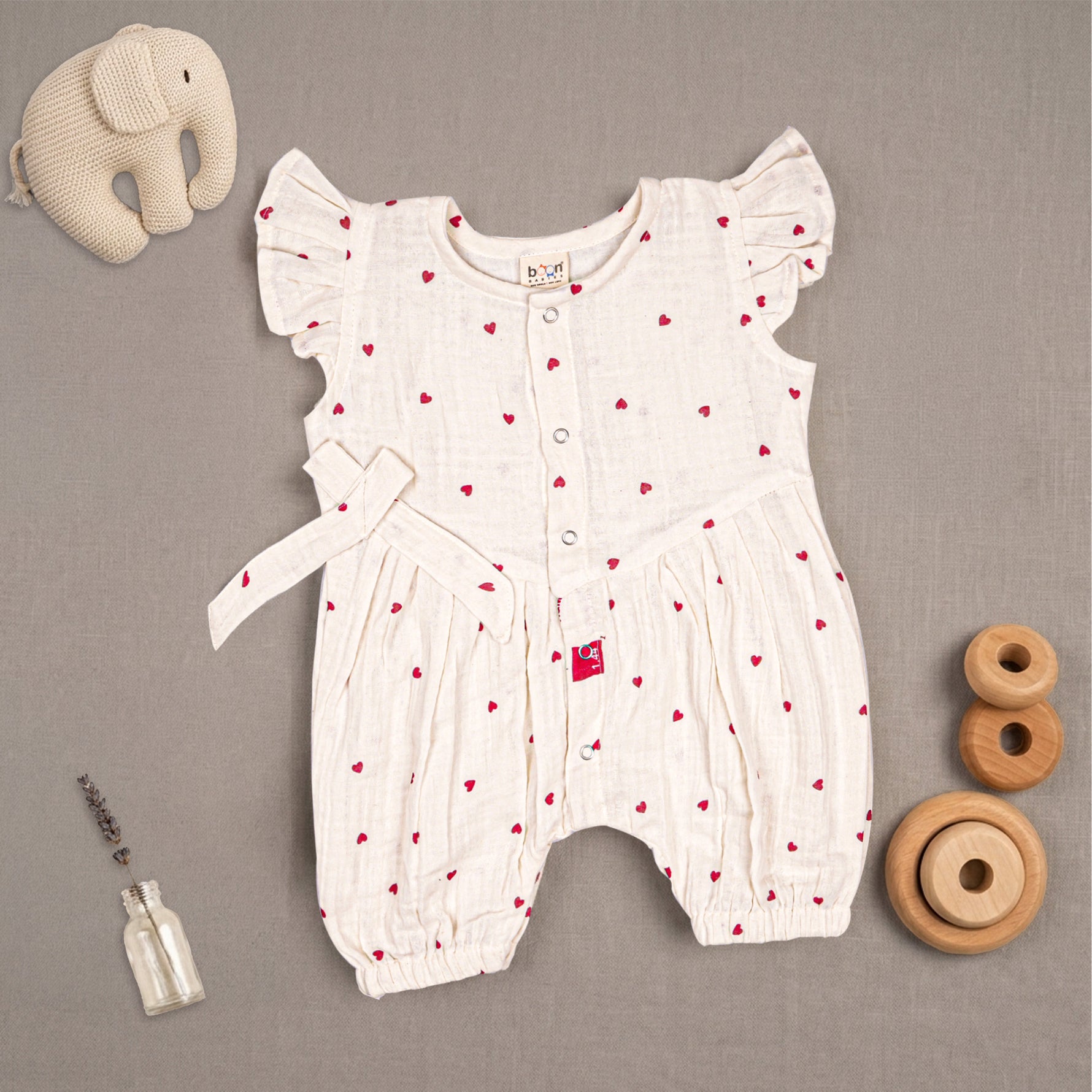 Baby girl wearing a Boon Babies muslin printed romper with frill sleeves, featuring a colorful floral pattern and soft fabric.