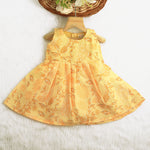 Sunshine yellow sleeveless slub cotton frock for baby girls with all-over orange floral print and pleated skirt, displayed flat on a white fur background with floral basket hanger.