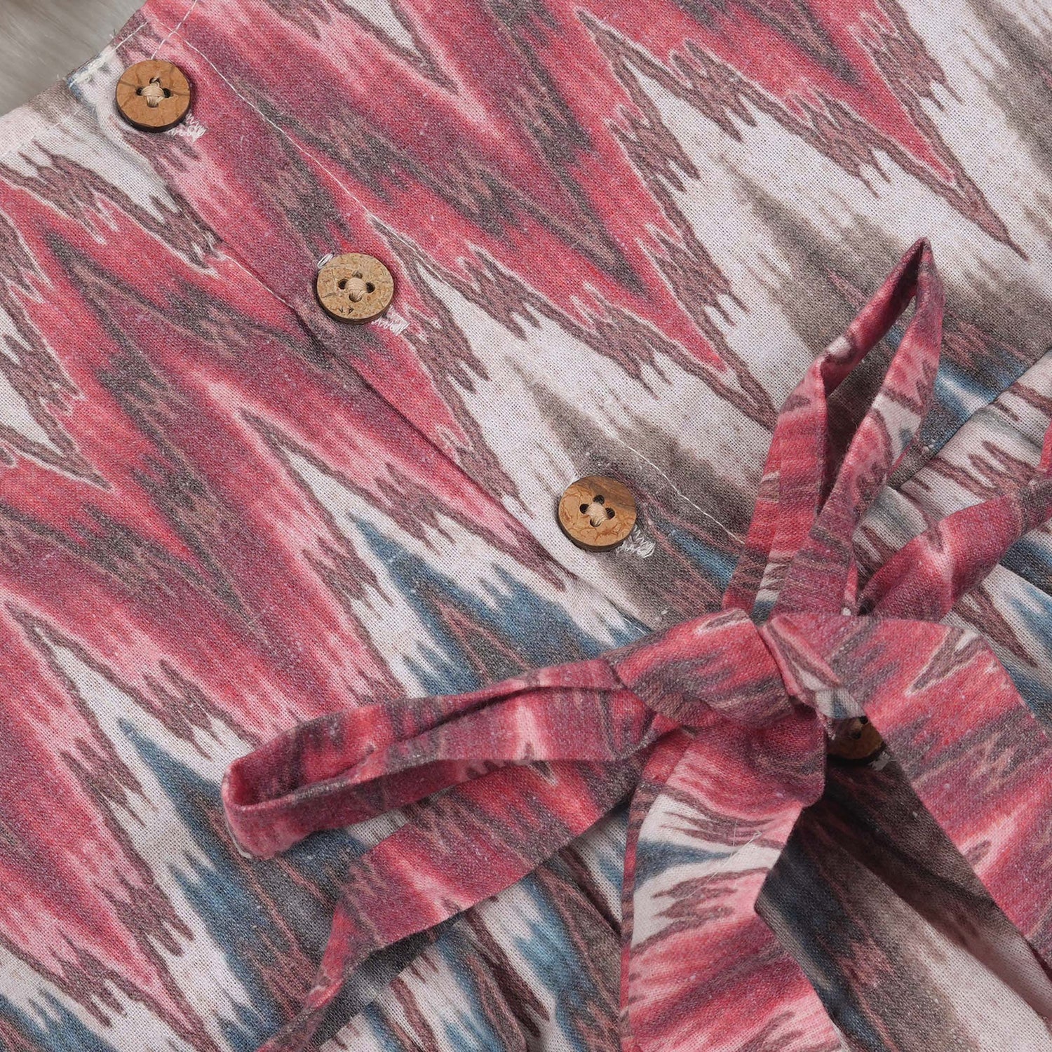 Girls’ sleeveless frock in multicolor Ikat print, made from cotton – displayed flat on white fur background with floral props – Boon Babies casual summer wear for girls aged 12M to 5Y.
