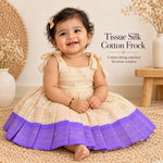 Baby girl wearing cream tissue silk cotton knot frock with purple border and gold woven motifs
