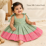 Baby girl wearing sage green tissue silk cotton knot frock with pink border and gold woven motifs