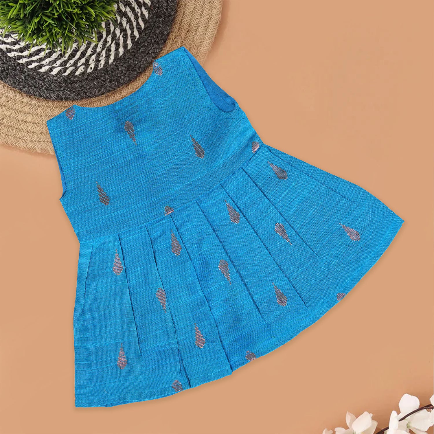 Blue silk sleeveless ethnic frock for baby girls with wooden buttons and traditional motifs, laid flat on a beige background with rustic and floral decor.