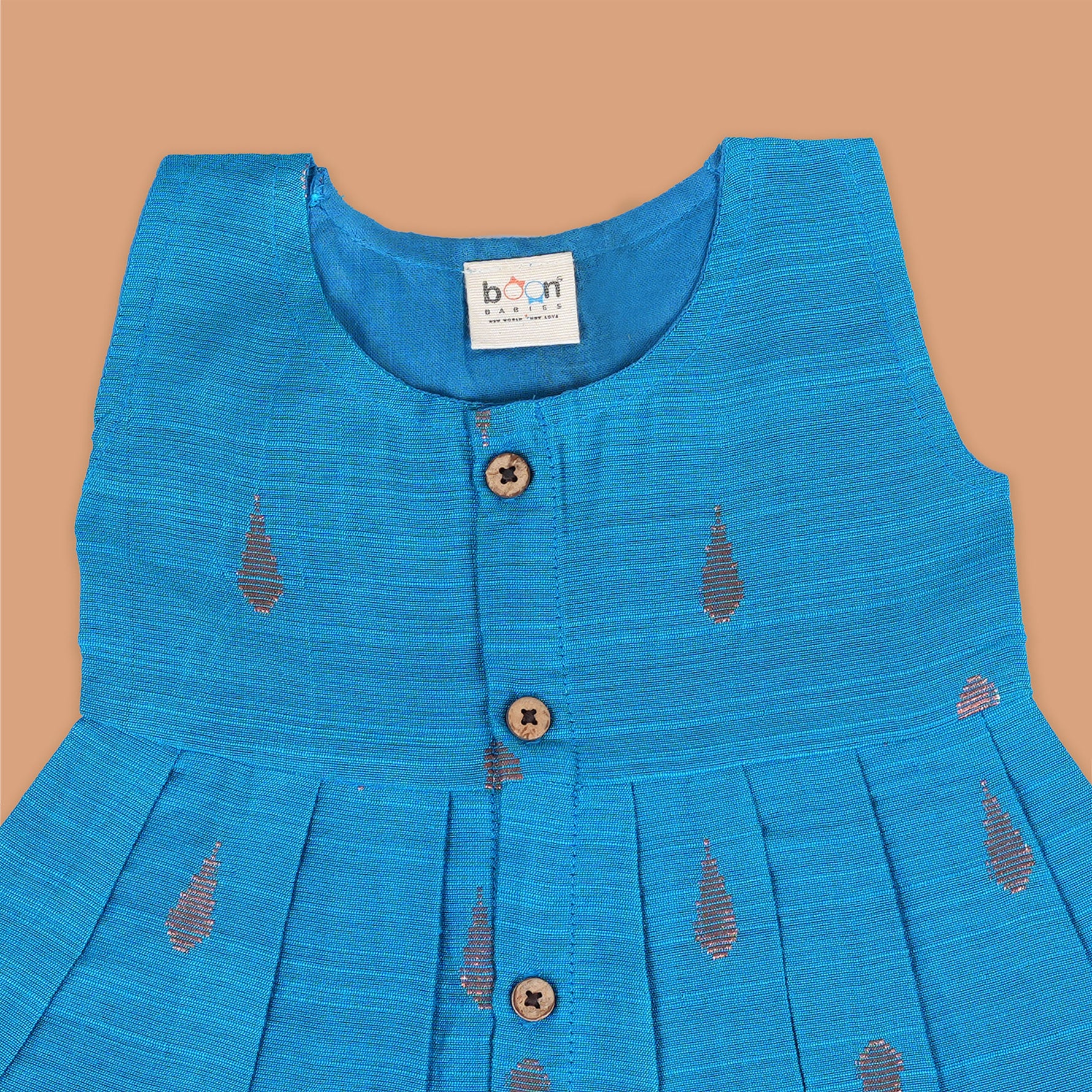 Blue silk sleeveless ethnic frock for baby girls with wooden buttons and traditional motifs, laid flat on a beige background with rustic and floral decor.