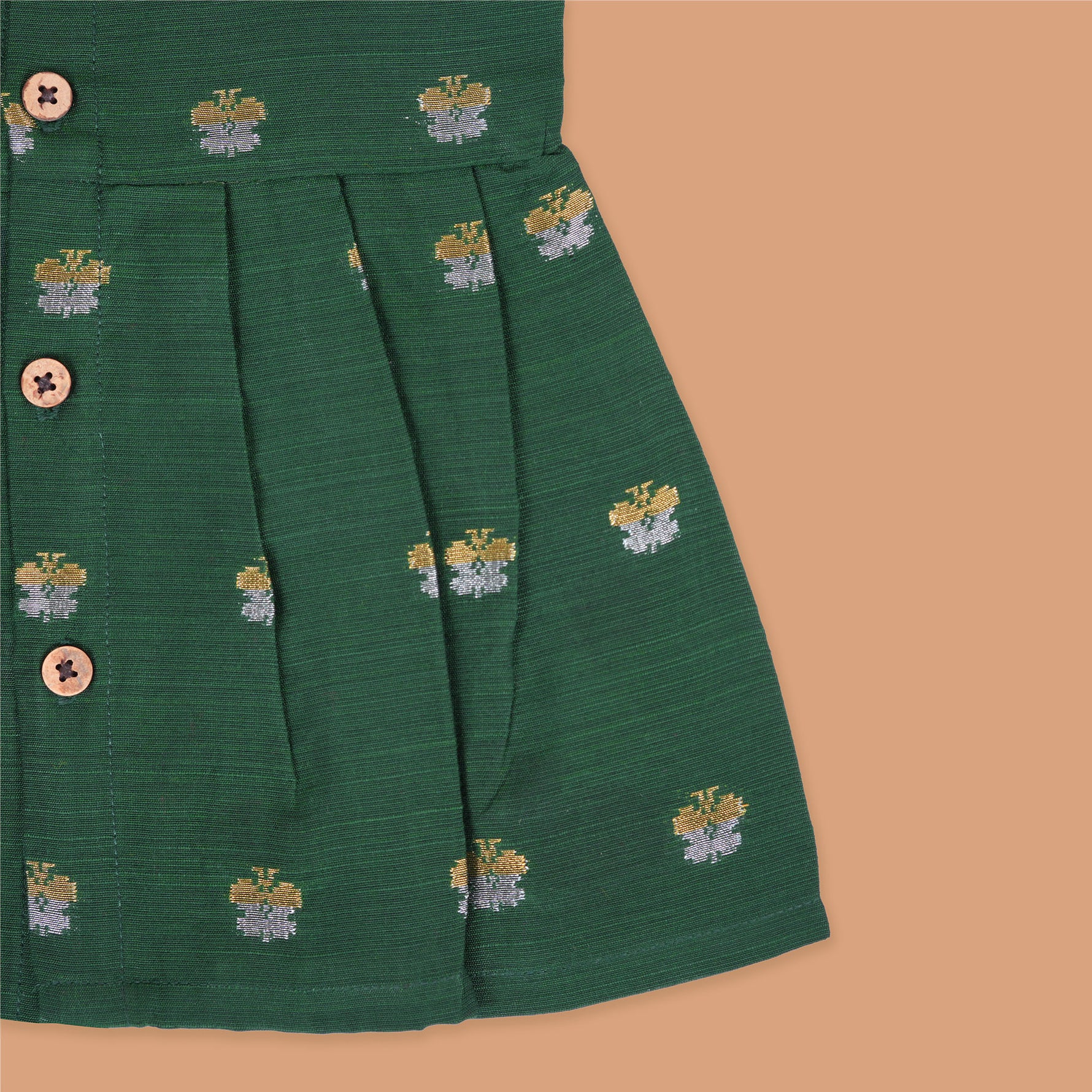 Floral green silk sleeveless frock for baby girls with wooden buttons and subtle motifs, displayed on a beige backdrop with soft floral accents and woven mat.