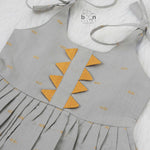 Festive grey silk Onam knot frock with triangle yoke design & zari border. Perfect for baby girls (0–12M).