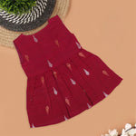 Maroon sleeveless ethnic silk frock for baby girls with wooden buttons and traditional motifs, displayed on a beige background with rustic mats and floral accents.