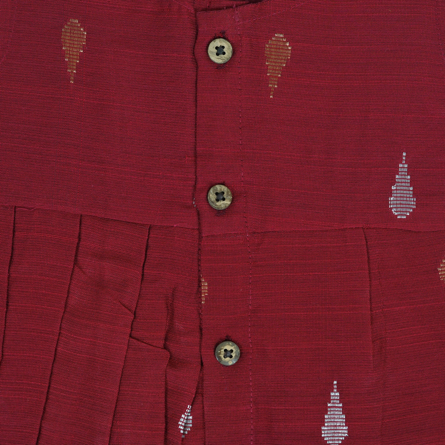 Maroon sleeveless ethnic silk frock for baby girls with wooden buttons and traditional motifs, displayed on a beige background with rustic mats and floral accents.
