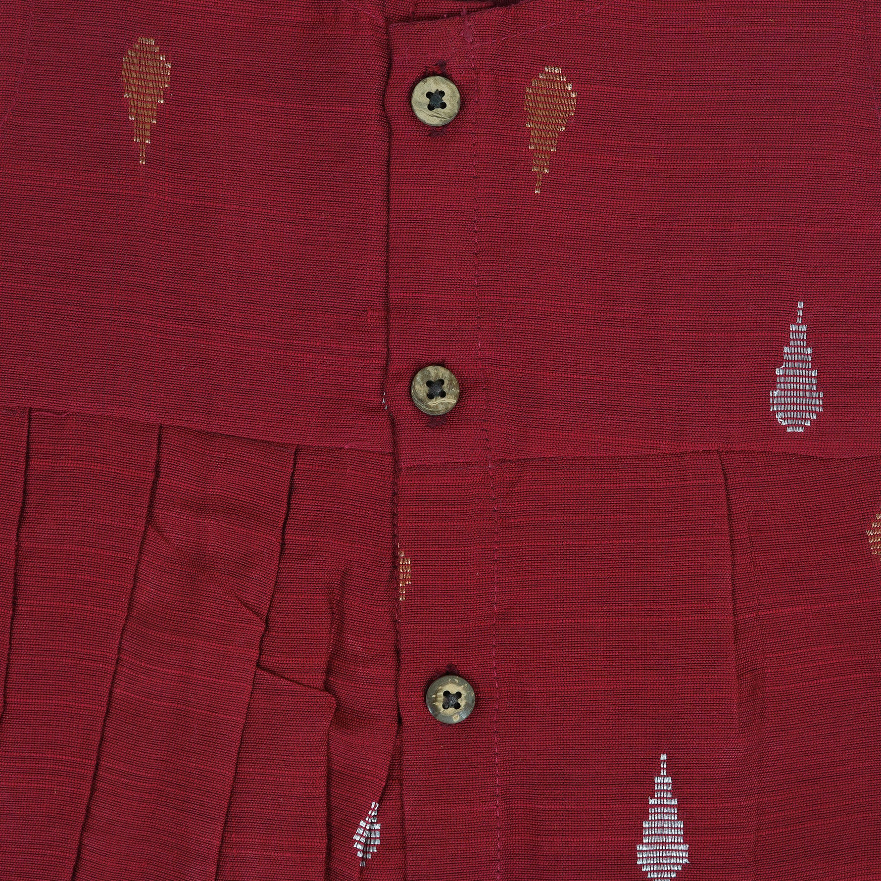 Maroon sleeveless ethnic silk frock for baby girls with wooden buttons and traditional motifs, displayed on a beige background with rustic mats and floral accents.