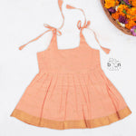 Peach silk Onam knot frock with zari border & triangle yoke. Ages 0–12M. Elegant festive outfit for baby girls.