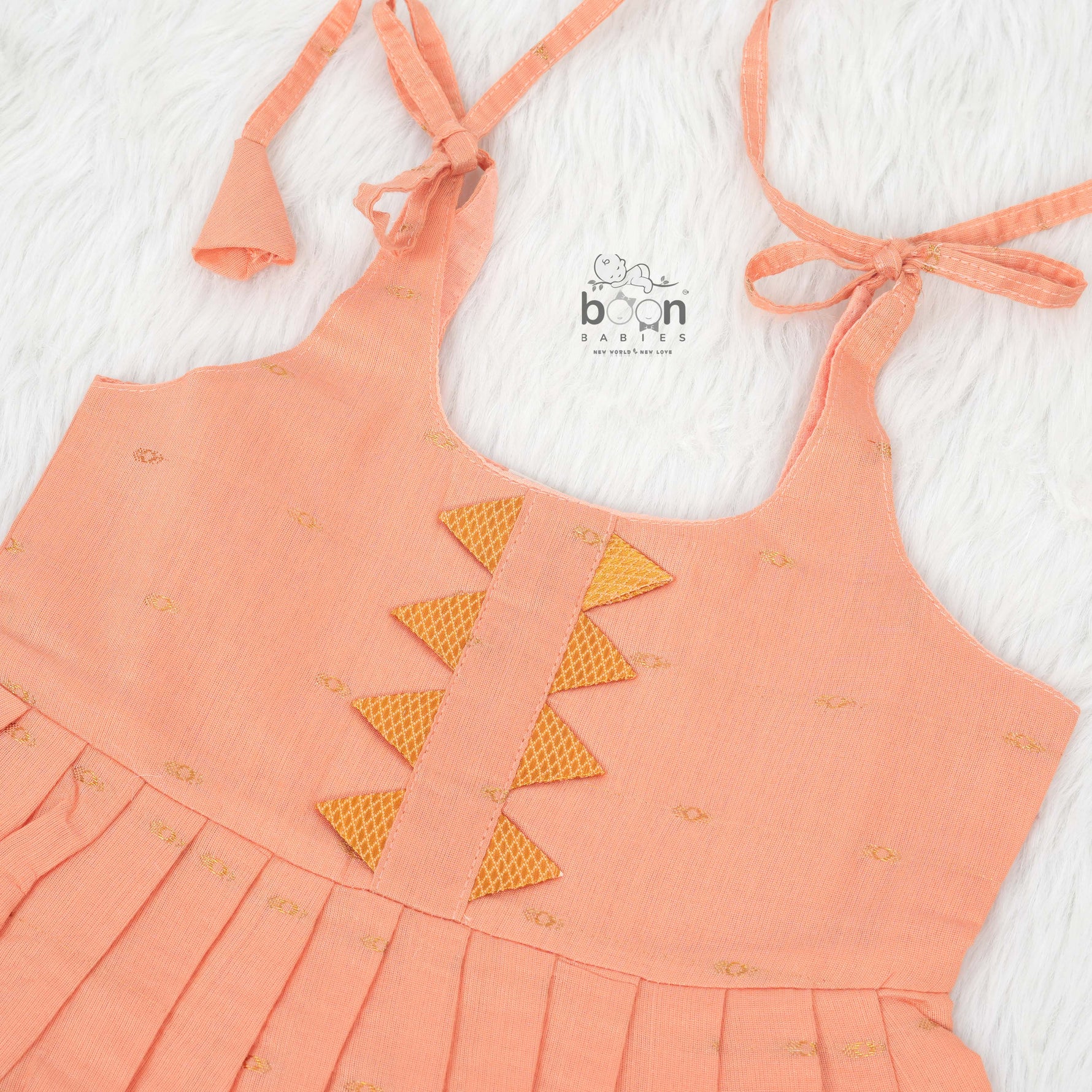 Peach silk Onam knot frock with zari border & triangle yoke. Ages 0–12M. Elegant festive outfit for baby girls.