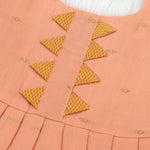 Peach silk Onam knot frock with zari border & triangle yoke. Ages 0–12M. Elegant festive outfit for baby girls.