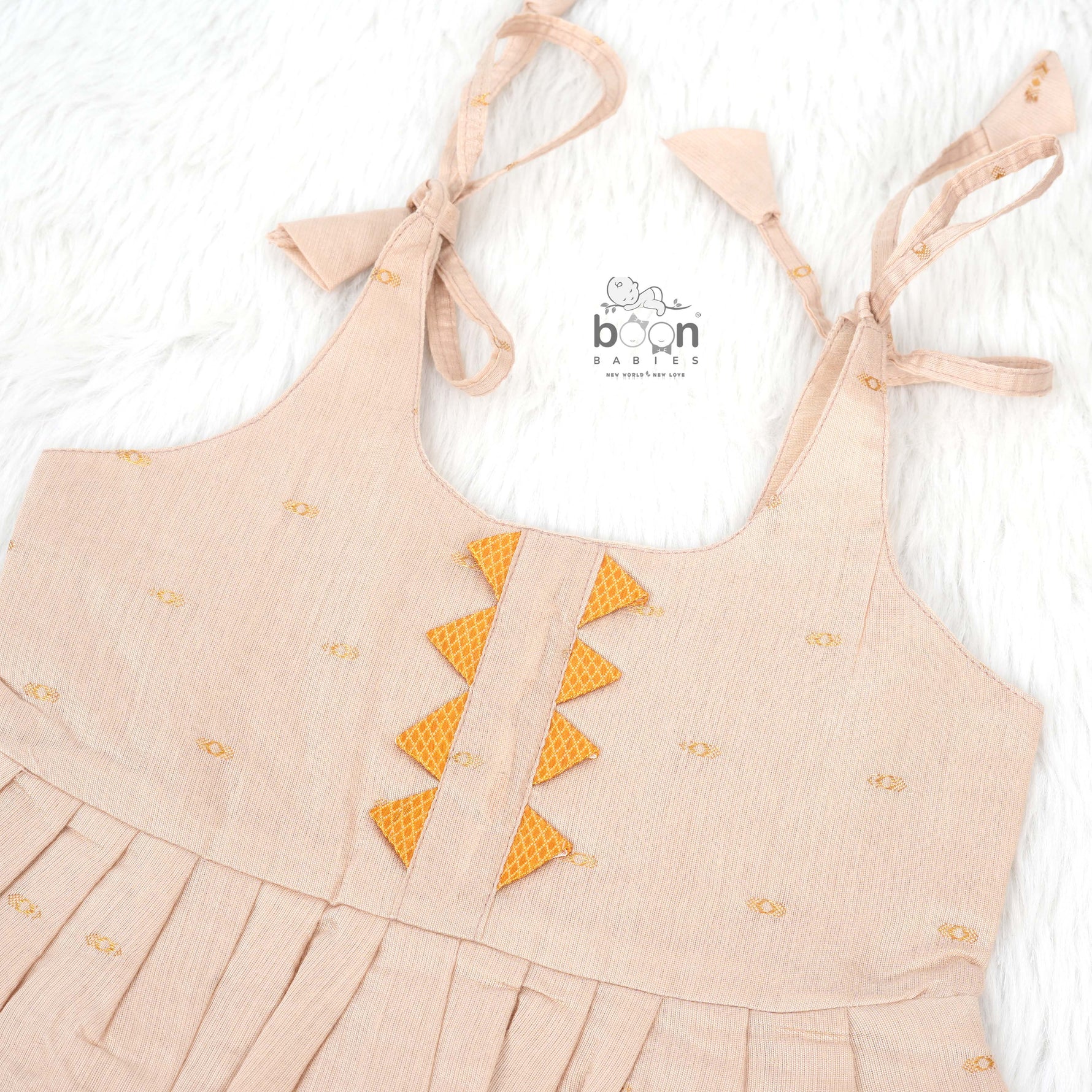 Beige silk Onam knot frock with zari border & triangle yoke. Ages 0–12M. Elegant festive outfit for baby girls.