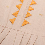 Beige silk Onam knot frock with zari border & triangle yoke. Ages 0–12M. Elegant festive outfit for baby girls.