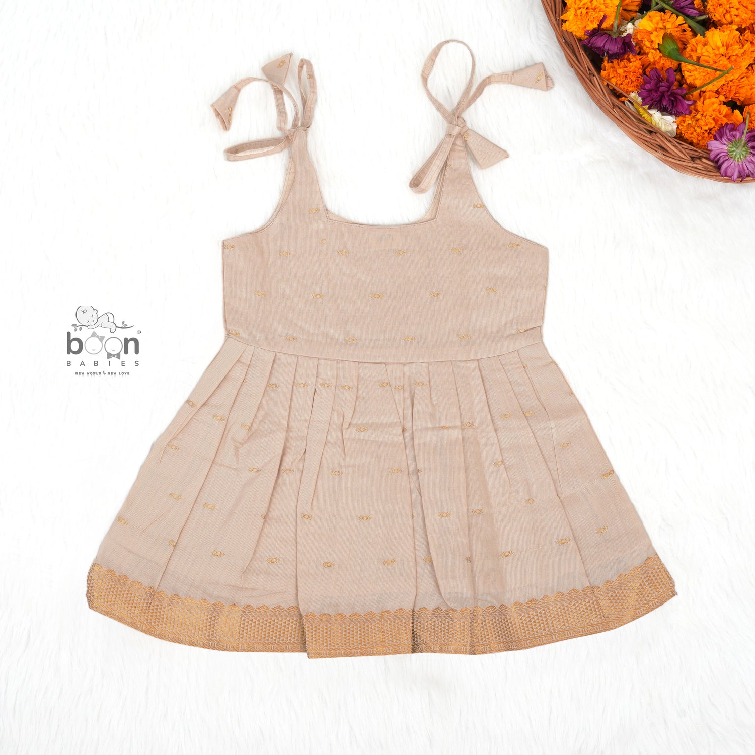 Beige silk Onam knot frock with zari border & triangle yoke. Ages 0–12M. Elegant festive outfit for baby girls.