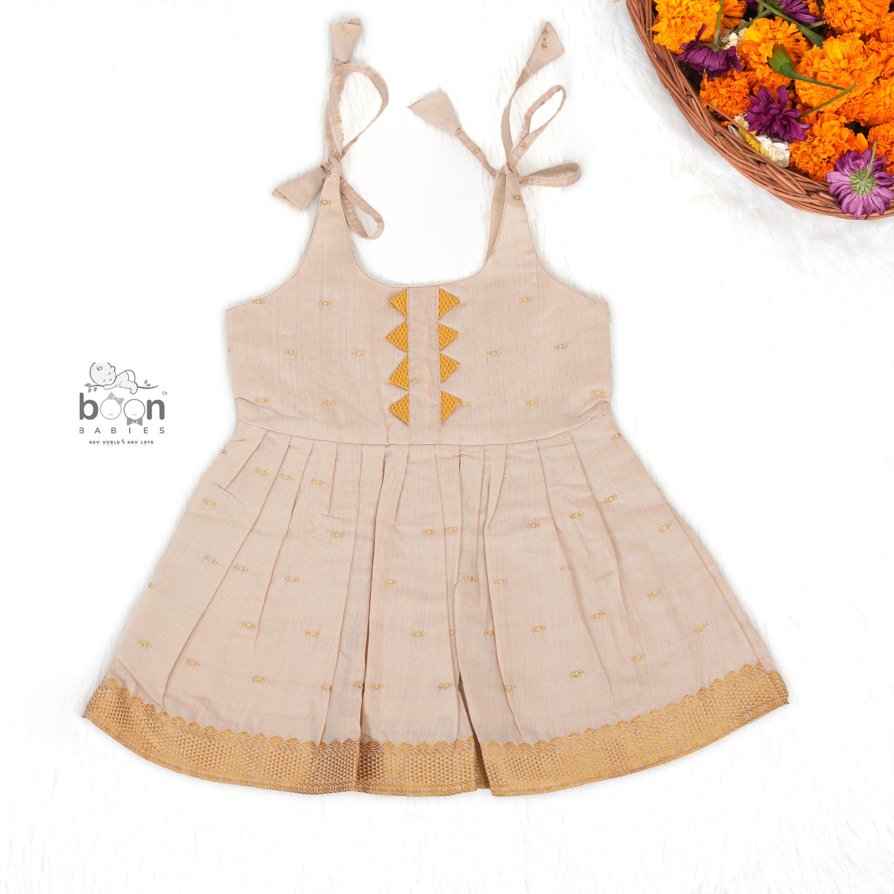 Beige silk Onam knot frock with zari border & triangle yoke. Ages 0–12M. Elegant festive outfit for baby girls.