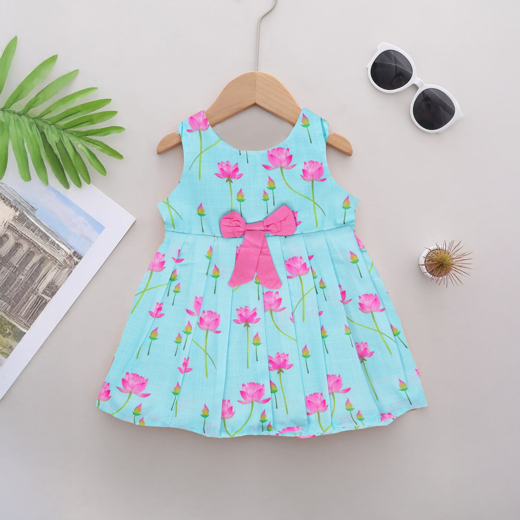 Adorable sleeveless cotton frock with pink lotus prints & bow. Ages 1–4 years. Comfortable, stylish & perfect for festive and casual occasions.