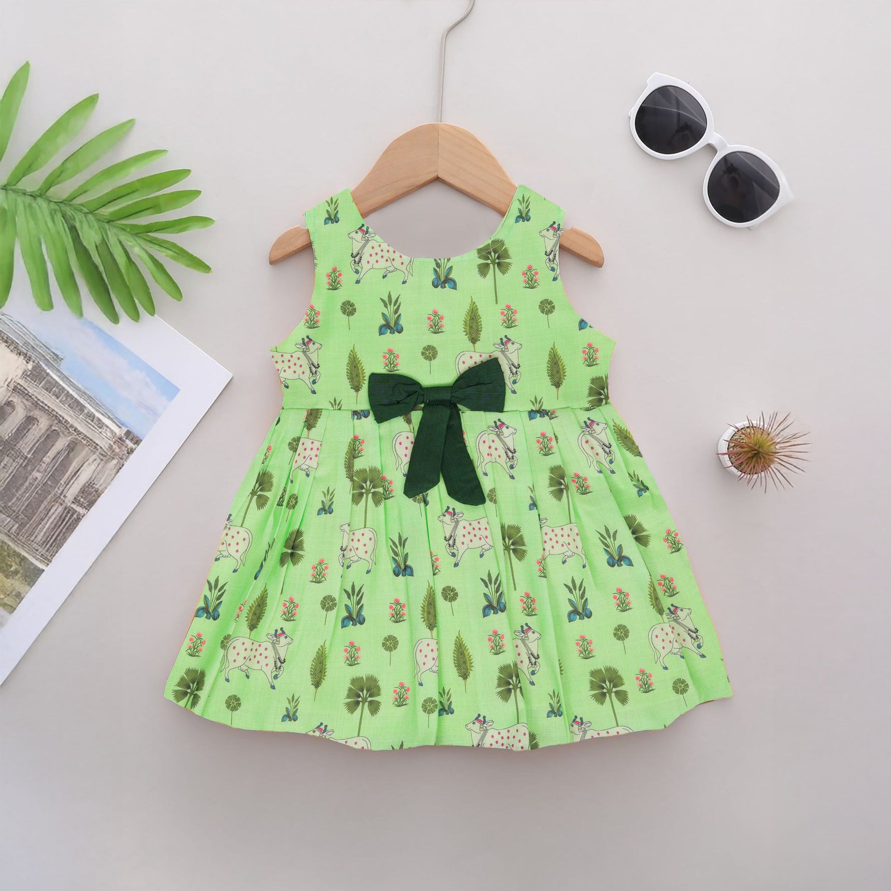 Cute sleeveless cotton frock in green with deer & floral prints. Ages 1–4 years. Soft, breathable & perfect for festive and casual looks.