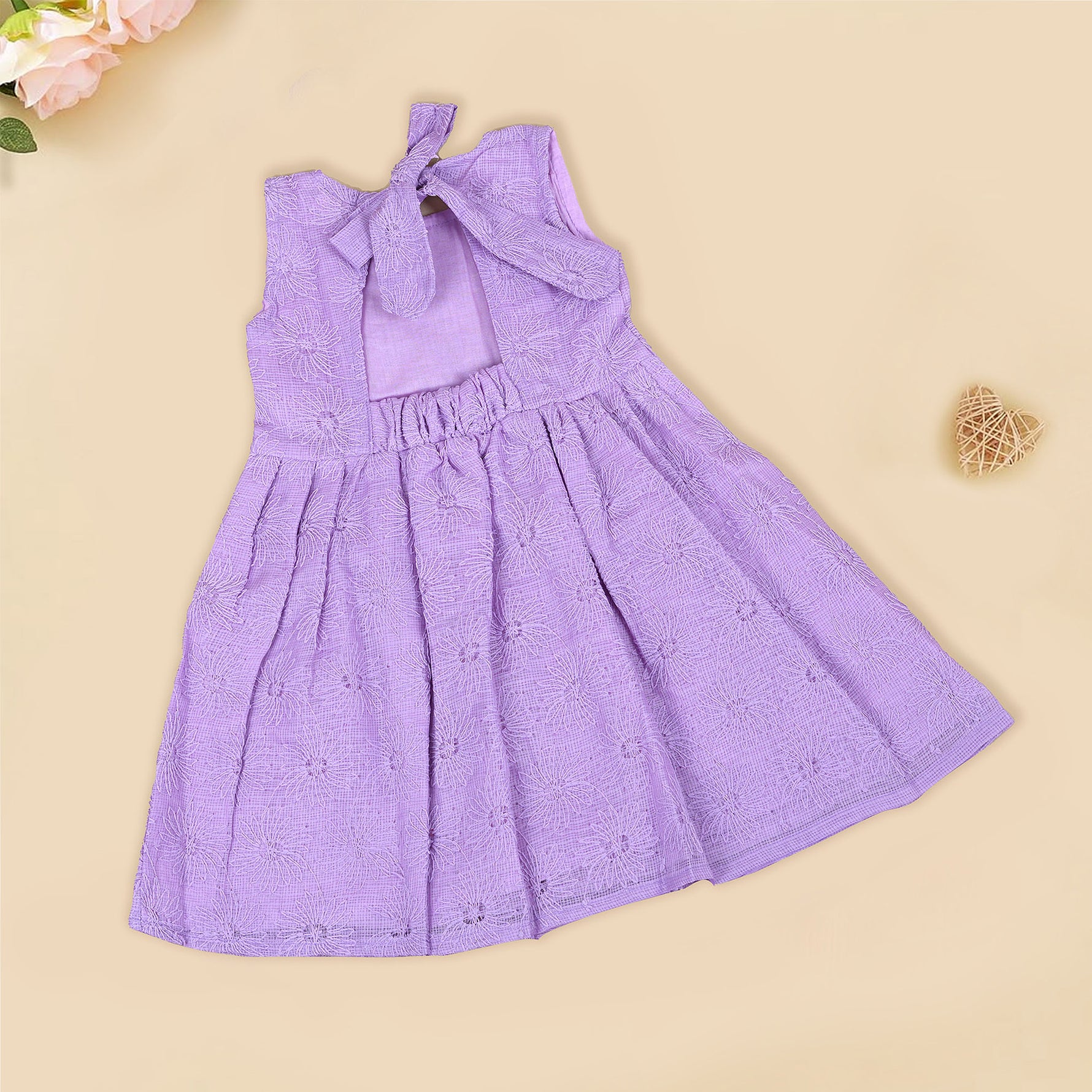 Lilac sleeveless Hakoba frock for baby girls, featuring floral embroidery and soft pleats, displayed flat on a beige background with a decorative heart and flowers.