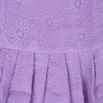 Lilac sleeveless Hakoba frock for baby girls, featuring floral embroidery and soft pleats, displayed flat on a beige background with a decorative heart and flowers.