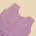 Mauve Hakoba frock for baby girls, sleeveless and pleated with soft embroidery, laid flat on a beige background beside floral accents and a heart-shaped wicker prop.