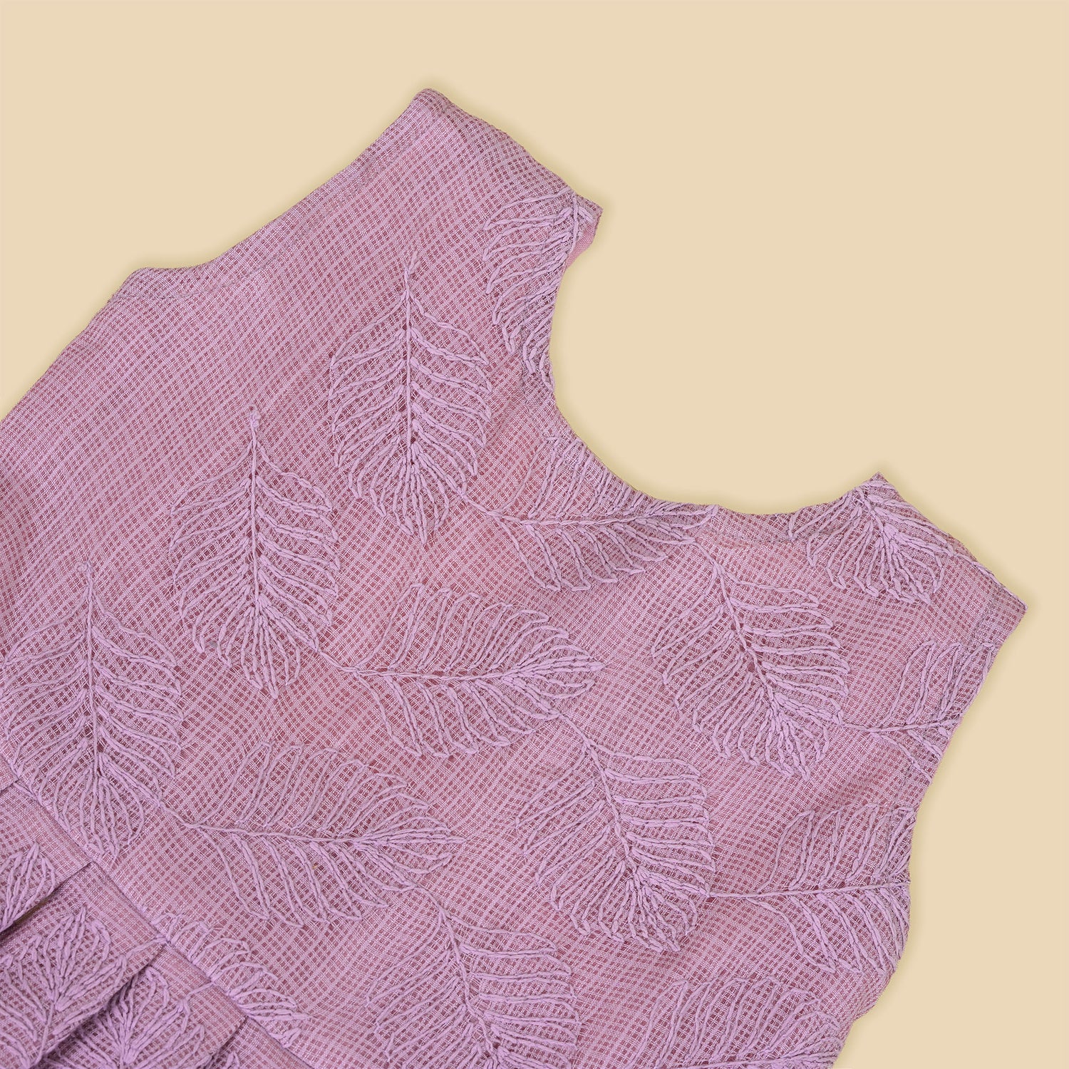 Mauve Hakoba frock for baby girls, sleeveless and pleated with soft embroidery, laid flat on a beige background beside floral accents and a heart-shaped wicker prop.