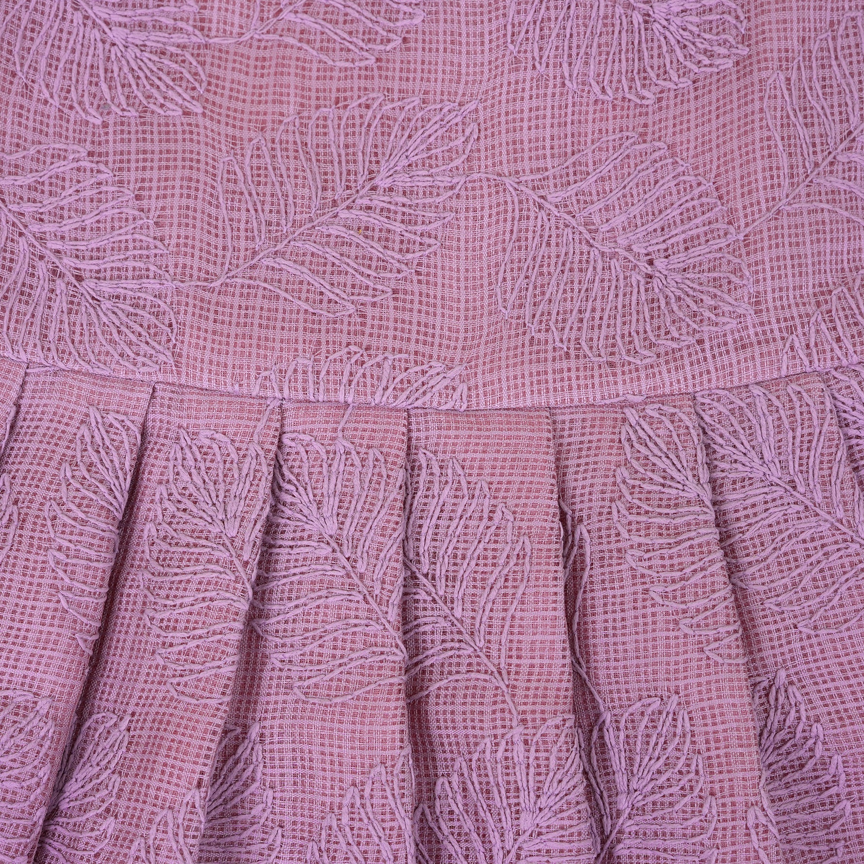 Mauve Hakoba frock for baby girls, sleeveless and pleated with soft embroidery, laid flat on a beige background beside floral accents and a heart-shaped wicker prop.