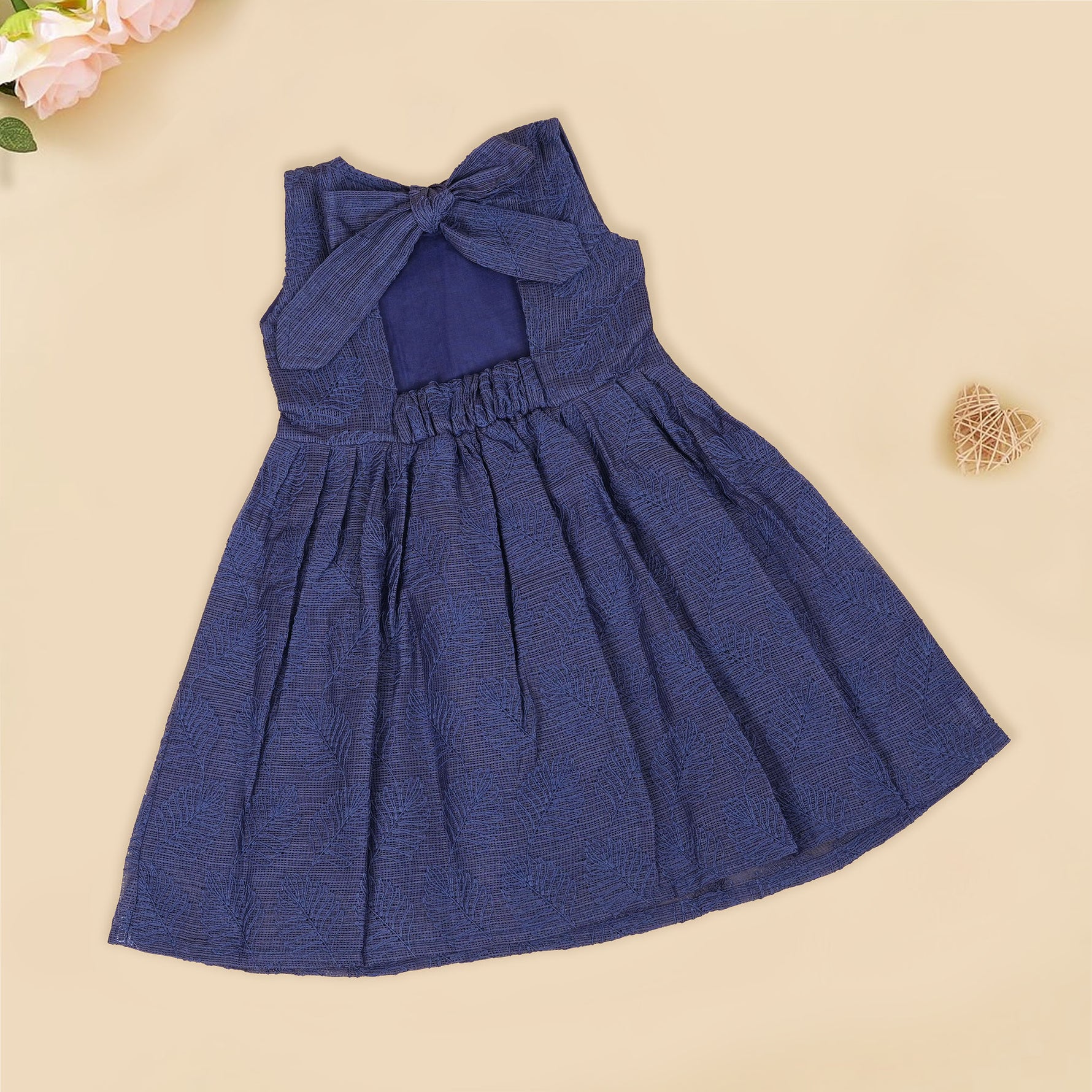 Navy blue sleeveless Hakoba frock for baby girls, featuring soft floral embroidery and pleated cotton design, placed flat on a beige backdrop with heart-shaped decor.