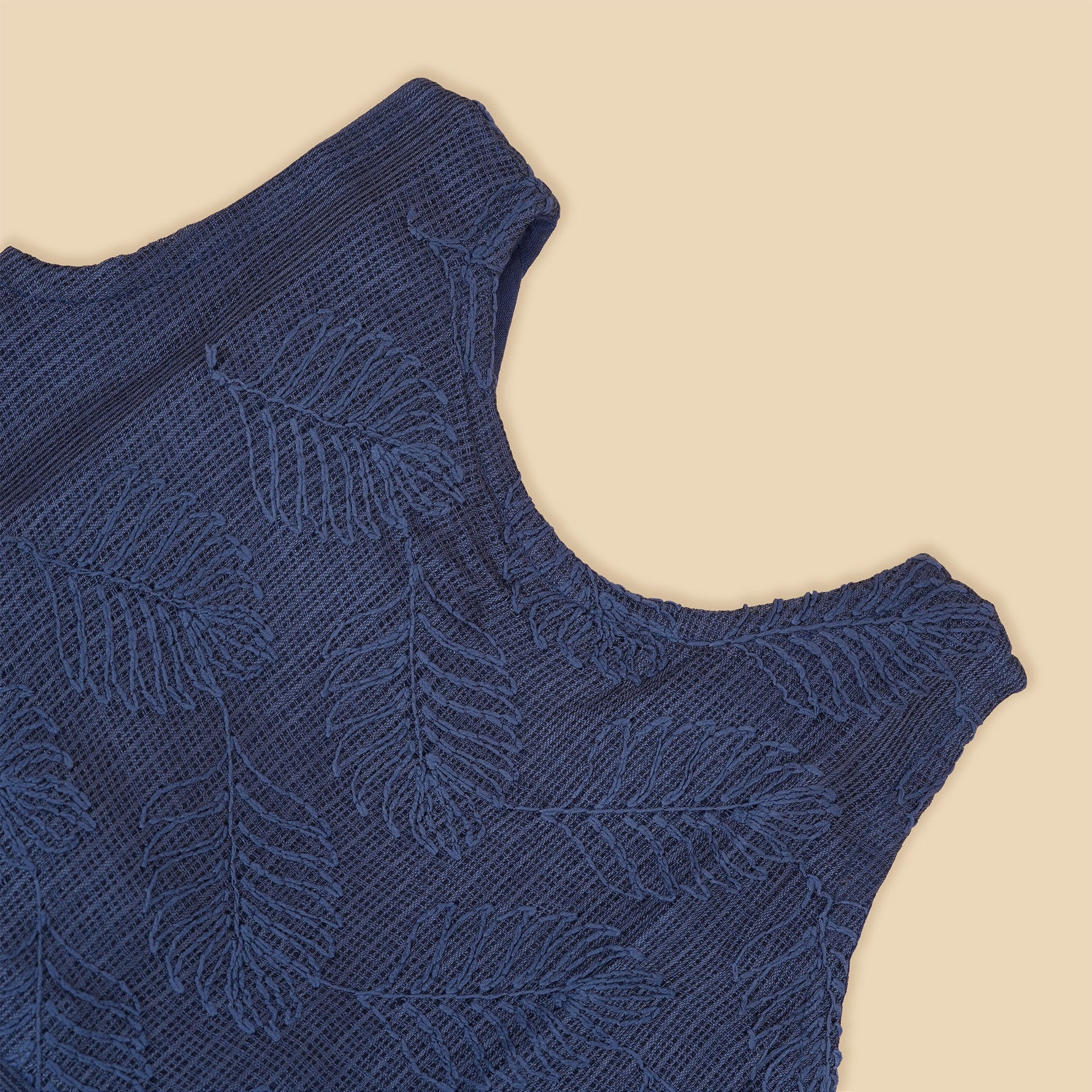 Navy blue sleeveless Hakoba frock for baby girls, featuring soft floral embroidery and pleated cotton design, placed flat on a beige backdrop with heart-shaped decor.