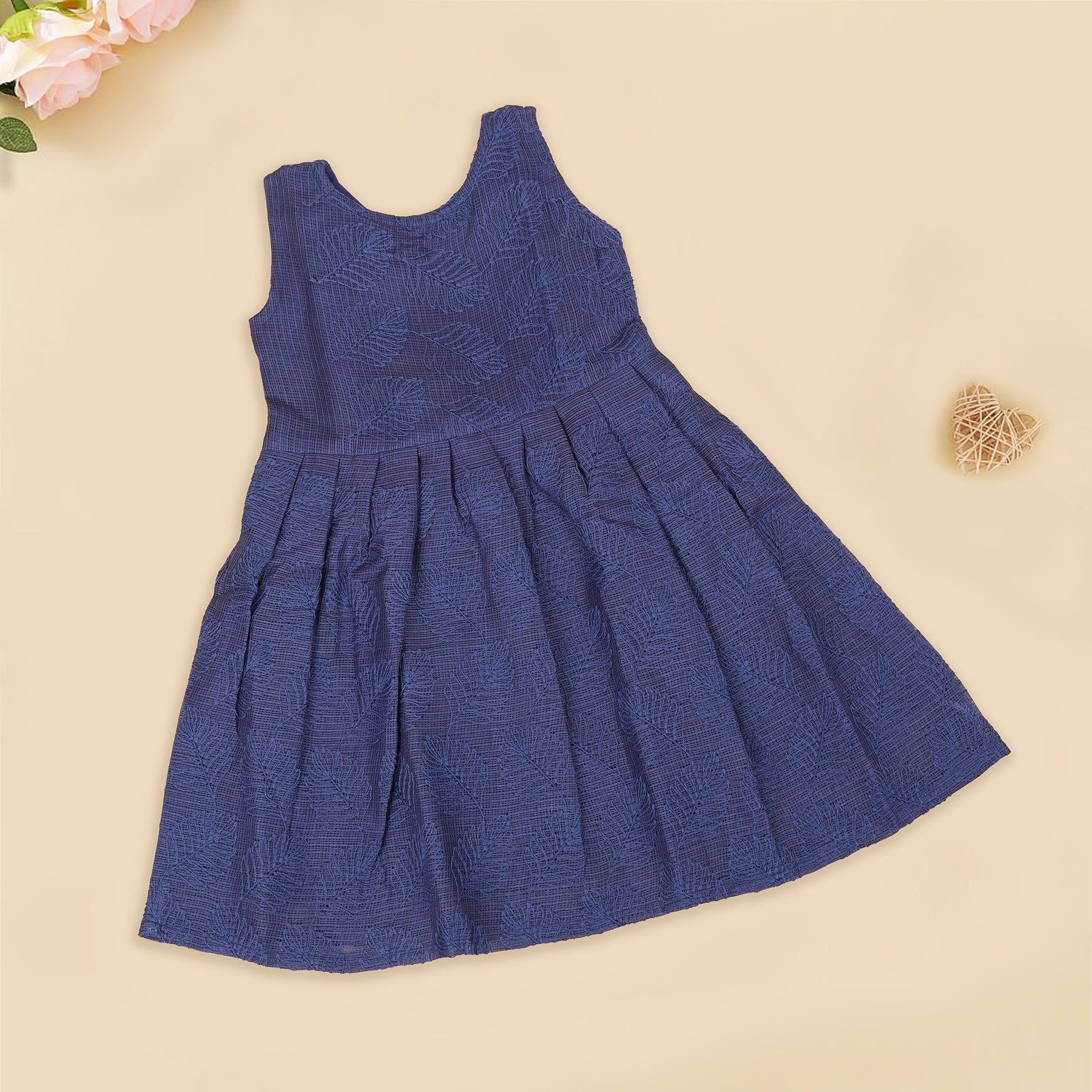 Navy blue sleeveless Hakoba frock for baby girls, featuring soft floral embroidery and pleated cotton design, placed flat on a beige backdrop with heart-shaped decor.