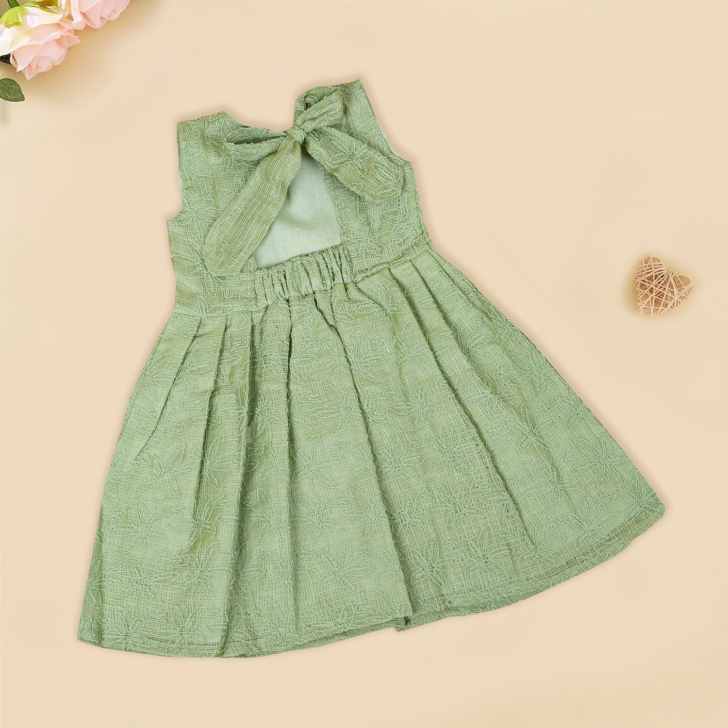 Pastel green sleeveless Hakoba frock for baby girls, featuring floral embroidery and pleated skirt design. Lightweight cotton fabric, displayed flat against a soft beige background with a decorative heart and flowers.