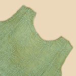 Pastel green sleeveless Hakoba frock for baby girls, featuring floral embroidery and pleated skirt design. Lightweight cotton fabric, displayed flat against a soft beige background with a decorative heart and flowers.