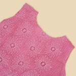 Pink sleeveless Hakoba frock for baby girls, featuring floral embroidery and pleated skirt design, laid flat on a beige background with soft floral props.