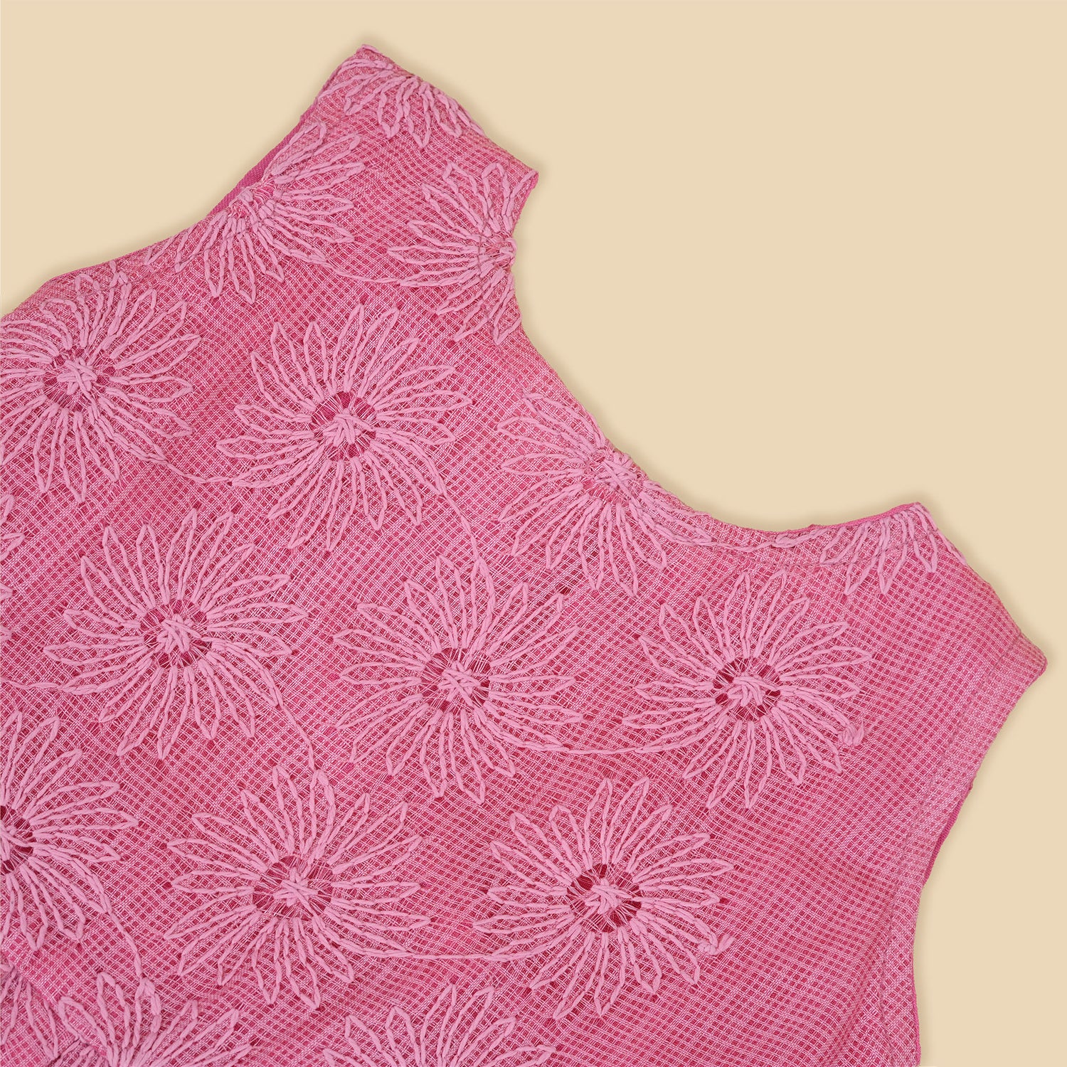 Pink sleeveless Hakoba frock for baby girls, featuring floral embroidery and pleated skirt design, laid flat on a beige background with soft floral props.