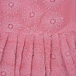 Pink sleeveless Hakoba frock for baby girls, featuring floral embroidery and pleated skirt design, laid flat on a beige background with soft floral props.