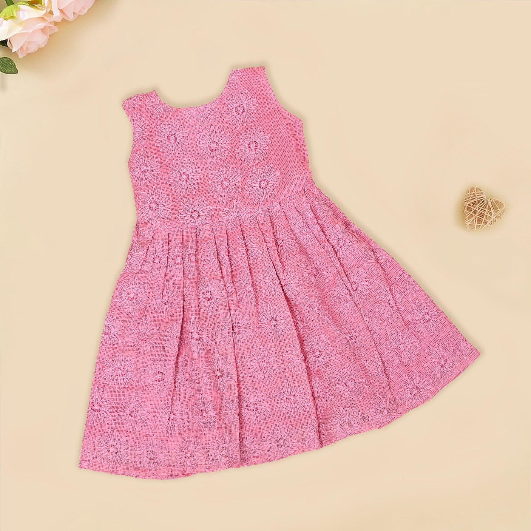 Pink sleeveless Hakoba frock for baby girls, featuring floral embroidery and pleated skirt design, laid flat on a beige background with soft floral props.