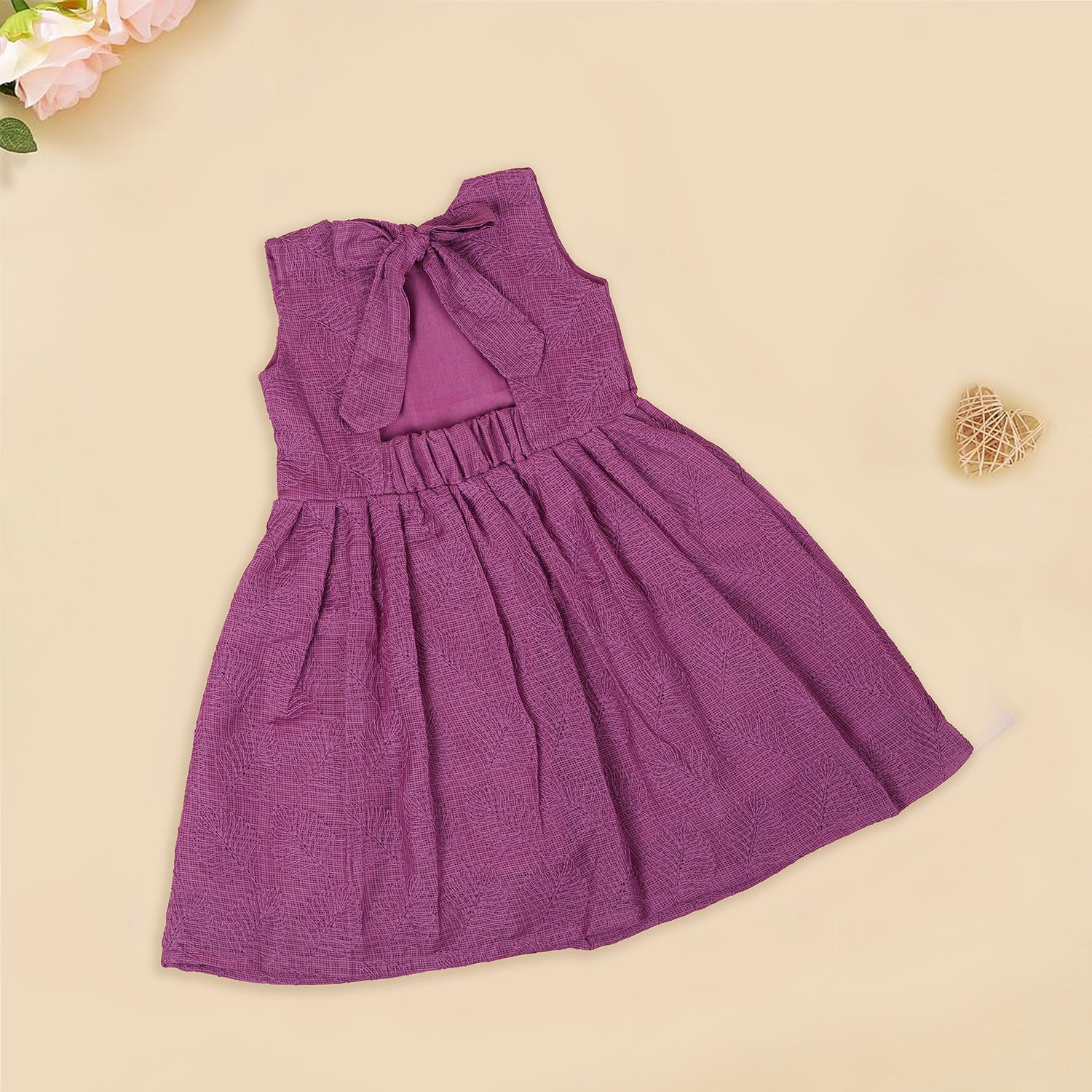 Wine-colored Hakoba frock for baby girls with sleeveless cut, floral embroidery, and pleated skirt design, laid flat on a beige background with floral props.