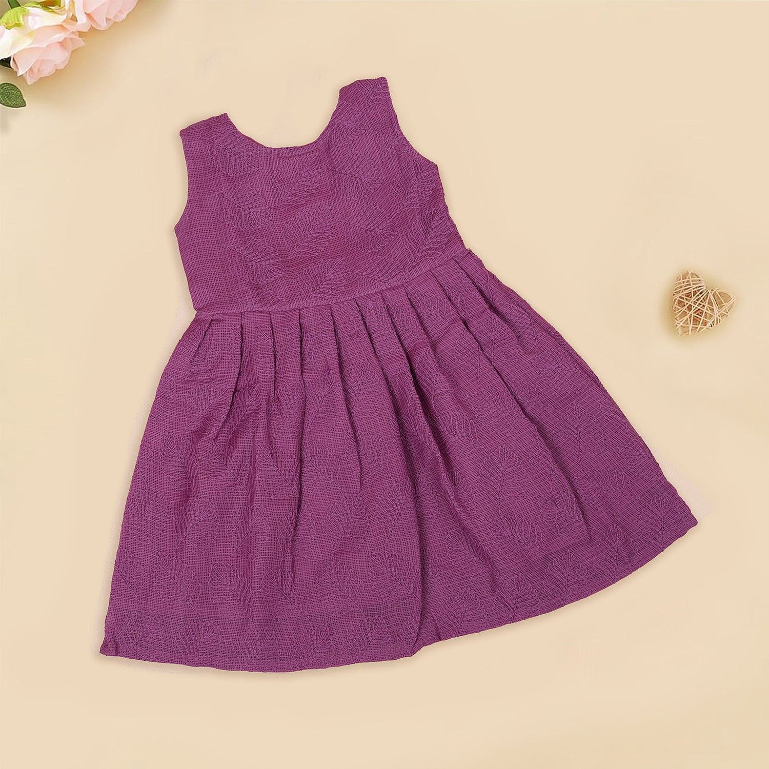 Wine-colored Hakoba frock for baby girls with sleeveless cut, floral embroidery, and pleated skirt design, laid flat on a beige background with floral props.