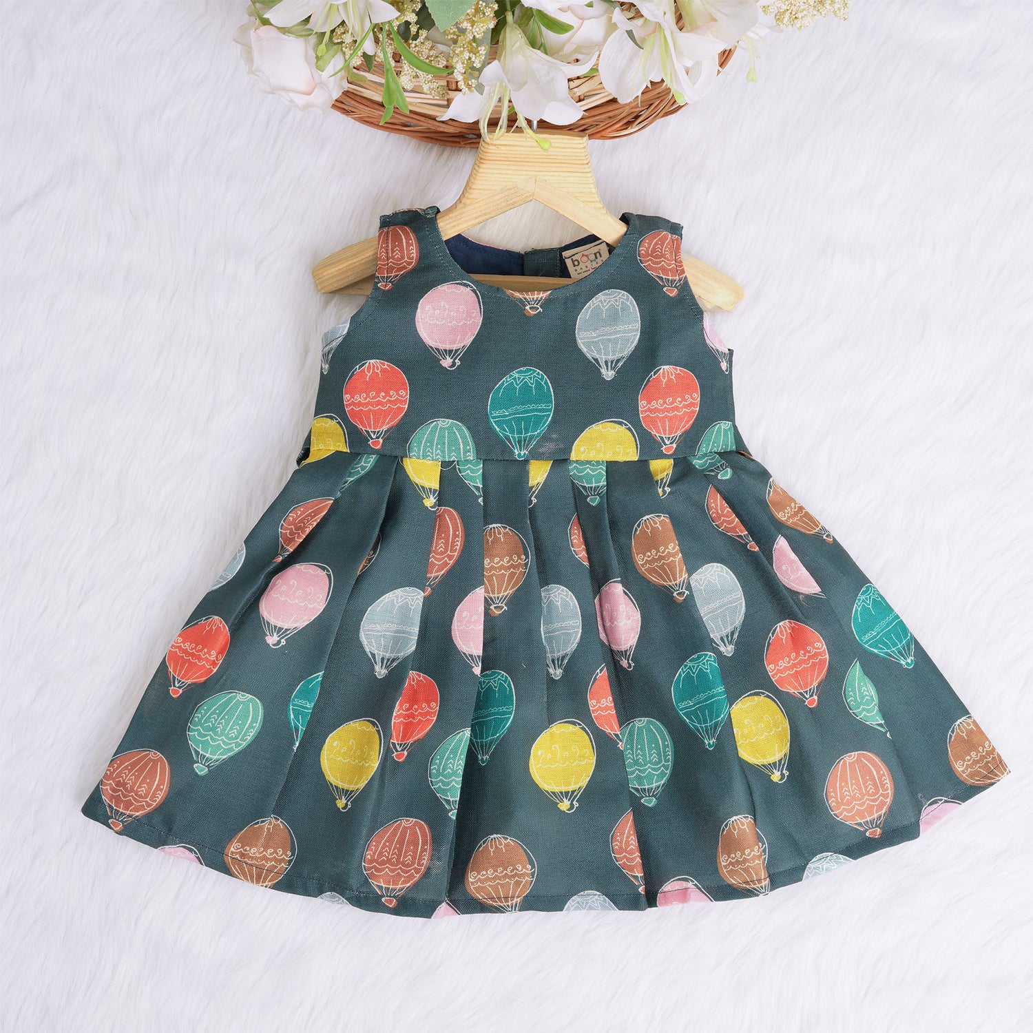 Little girl in a sleeveless denim blue frock with colorful balloon prints, made of slub cotton – part of Boon Babies babywear collection in Coimbatore.