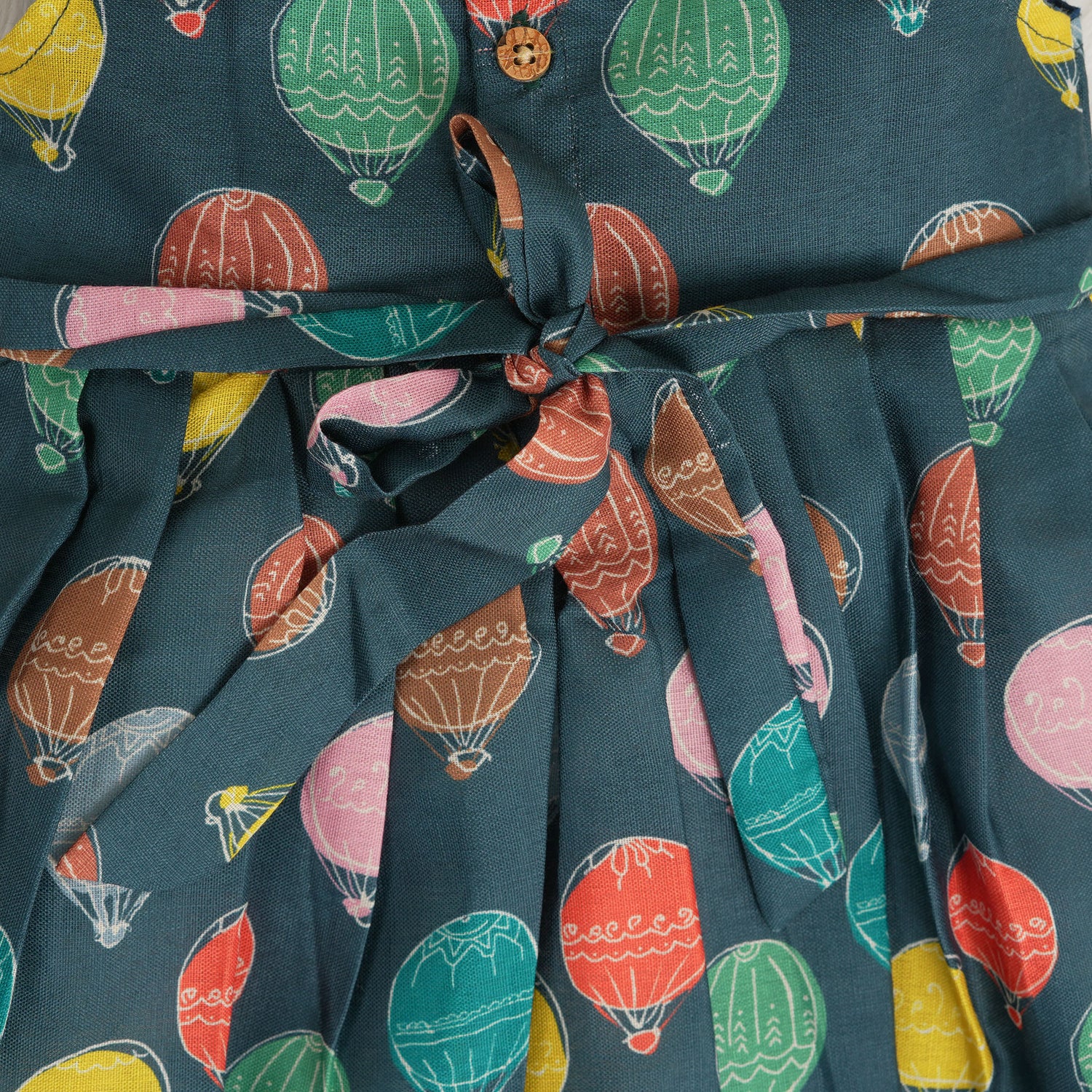 Little girl in a sleeveless denim blue frock with colorful balloon prints, made of slub cotton – part of Boon Babies babywear collection in Coimbatore.